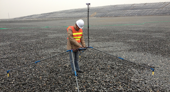 Photo of person using double dipole survey equipment on a soil-covered containment facility cell